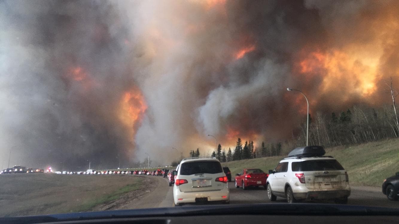 Bumper-to-bumper vehicles evacuating Fort McMurray on Highway 63 in May 2016 while wildfire smoke and flames rise on both sides of the road